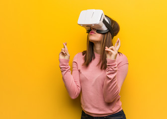 Young cute woman wearing a virtual reality googles crossing fingers for having luck