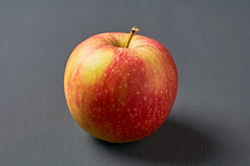 Single red fresh whole ripe apple full of vitamins lies on old dark scratched concrete table on kitchen. Harvest or diet concept. Close-up