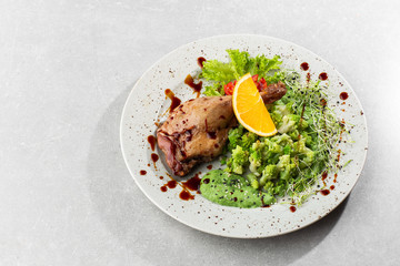 Roast duck leg with baked romanesco broccoli, lemon slice and chilli pepper on white plate, closeup. Horizontal view from above, top shot