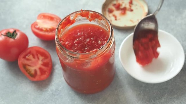 Female hand imposes tomato paste from a glass jar with a plate. Homemade canned tomatoes.