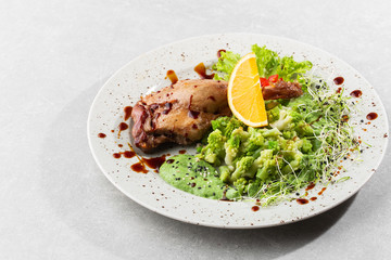 Roast duck leg with baked romanesco broccoli, lemon slice and chilli pepper on white plate, closeup. Horizontal view from above, top shot