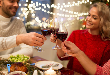 holidays and celebration concept - close up of happy friends having christmas dinner at home, drinking red wine and clinking glasses