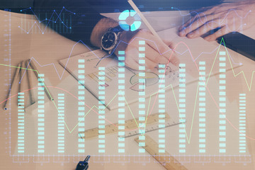 Double exposure of man's hands writing notes of stock market with forex chart.