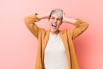 Young caucasian woman wearing a casual business clothes laughs joyfully keeping hands on head. Happiness concept.