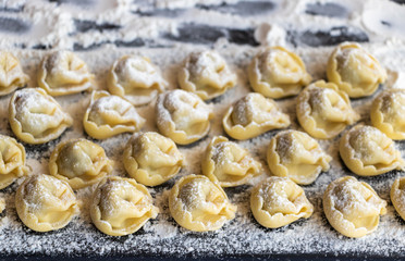 Tortellini sprinkled with flour on a dark board.