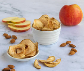 Apple chips near the almonds and apple on a marble background.
