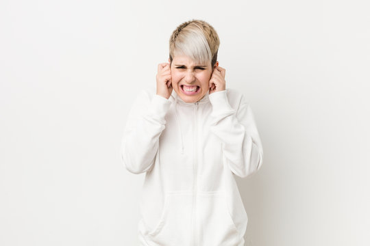 Young curvy woman wearing a white hoodie covering ears with hands.