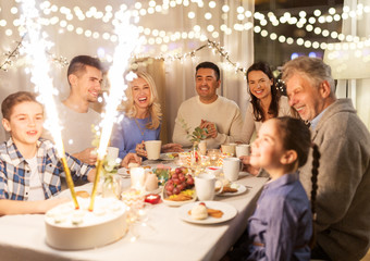 celebration, birthday and people concept - happy family having dinner party with fountain fireworks or sparkler candles burning on cake at home