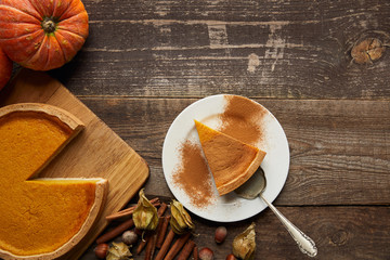 top view of pumpkin pie with cinnamon powder near whole pumpkin and spices on dark wooden surface