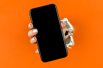 A woman holds a phone through ragged orange drywall.