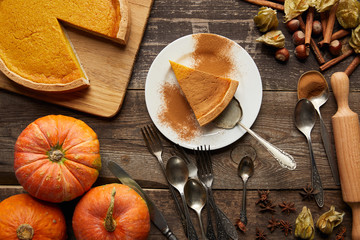 top view of tasty pumpkin pie on plate with spatula near whole pumpkins and cutlery on dark wooden surface