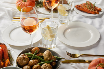 festive thanksgiving dinner with baked vegetables and glasses with rose wine and lemon water on white tablecloth