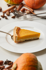 selective focus of tasty pumpkin pie near cutlery and spices isolated on grey