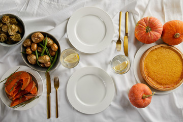 Fototapeta na wymiar top view of served dinner with pumpkin pie, baked vegetables and fresh whole pumpkins on white tablecloth