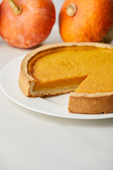 selective focus of delicious pumpkin pie near whole ripe pumpkins on white surface