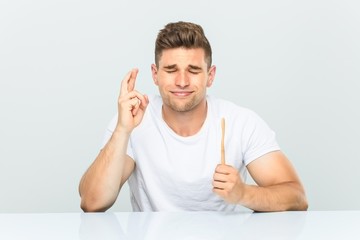 Young man holding a toothbrush crossing fingers for having luck