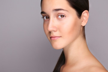 Portrait of young beautiful woman with perfectly clean face skin. Female with long black hair tied in ponytail smiling wide showing skincare results. Close up, copy space background.