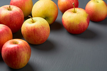 Lot of red fresh whole ripe apples full of vitamins scattered on old dark scratched concrete table on kitchen. Harvest or diet concept. Space for text