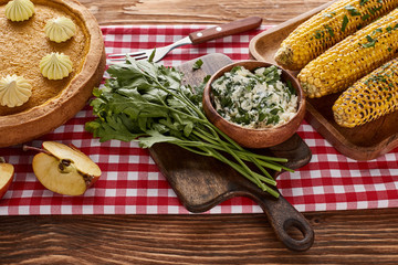 pumpkin pie, grilled corn and parsley on red checkered napkin at wooden table for Thanksgiving dinner
