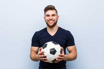 Young caucasian man holding a soccer ball happy, smiling and cheerful.