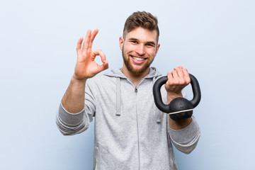 Young caucasian sportsman holding a dumbbell cheerful and confident showing ok gesture.