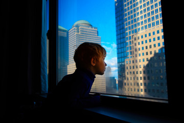 little boy looking at skyscrapers from the window