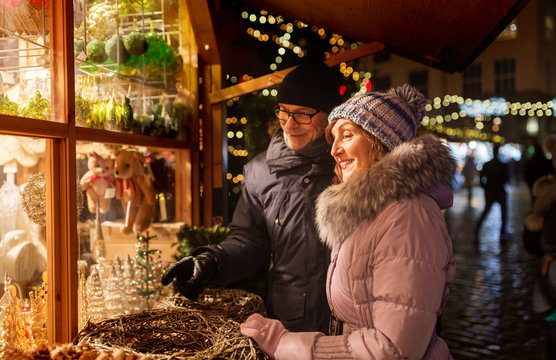shopping, winter holidays and people concept - happy senior couple at christmas market souvenir shop window on town hall square in tallinn, estonia
