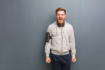 Young fitness redhead man screaming very angry and aggressive