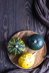 Autumn composition with small decorative pumpkins on a wooden plate, dark brown wooden background. 