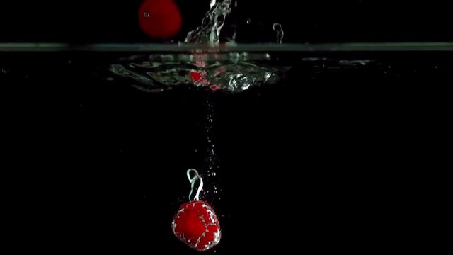 Raspberries splashing into water on black background closeup in super slow motion