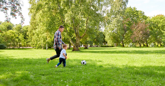 family, leisure and people concept - happy father and little son with ball playing soccer at summer park