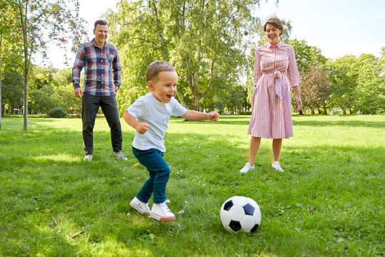 family, leisure and people concept - happy mother, father and little son with ball playing soccer at summer park