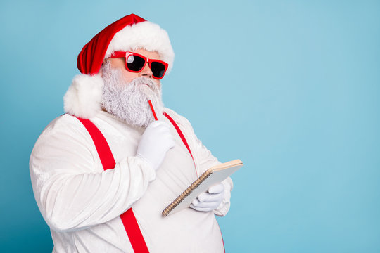 Close up photo of focused funny funky fat santa claus hold notebook think about wish list plan decide what choose look thoughtful wear stylish trendy suspenders isolated over blue color background