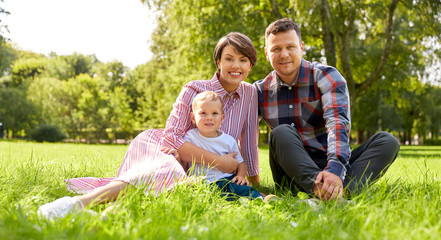 family, leisure and people concept - happy mother, father and little son at summer park sitting on grass