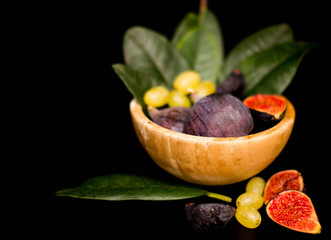 Fresh figs in a wooden plate, with grapes and leaves, shot low key. Vintage, close-up, top view.