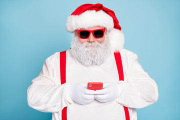 Close up photo of funny funky fat modern santa blogger in eyewear use cell phone type messages congratulations with christmas newyear wear overalls red suspenders isolated over blue color background