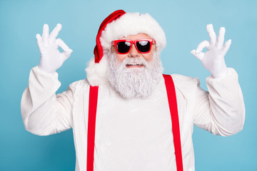 Close up photo of funny funky fat overweight hipster santa claus show ok okay sign recommend winter season shopping sales wear modern spectacles red suspenders isolated over blue color background