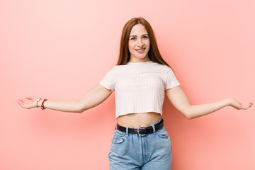 Young redhead ginger woman against a pink wall showing a welcome expression.
