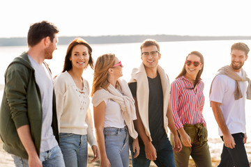 friendship, leisure and people concept - group of happy friends walking along beach in summer