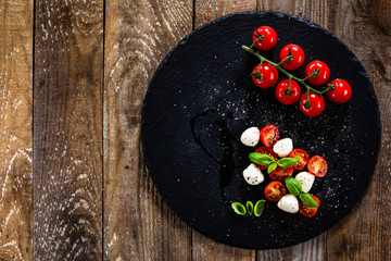 Caprese salad on black stone plate on wooden table