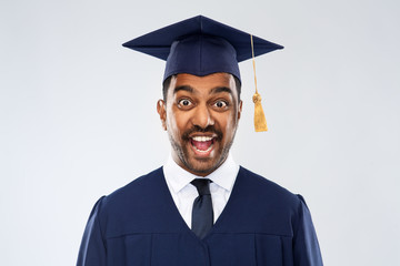 education, graduation and people concept - happy excited indian male graduate student in mortar board and bachelor gown over grey background