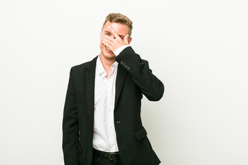 Young caucasian business man blink at the camera through fingers, embarrassed covering face.