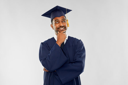 Education, Graduation And People Concept - Thinking Indian Male Graduate Student In Mortar Board And Bachelor Gown Over Grey Background