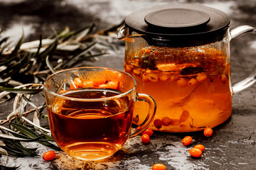 hot spicy tea with sea buckthorn in a glass teapot and Cup, on a dark background.
