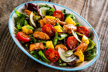 Salad with chicken, mango and tomatoes on wooden table