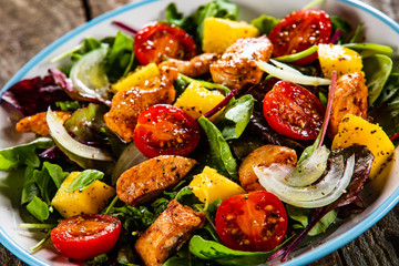 Salad with chicken, mango and tomatoes on wooden table
