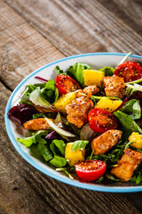 Salad with chicken, mango and tomatoes on wooden table