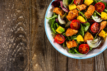 Salad with chicken, mango and tomatoes on wooden table