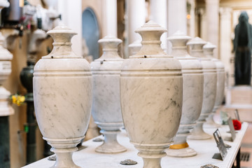 Set of white marble urns on top of a tomb with the cemetery in the background