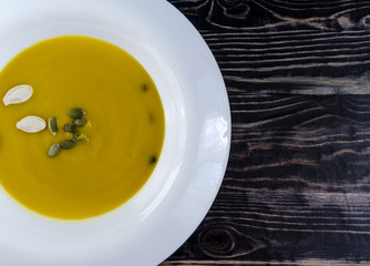 pumpkin soup in white plate natural wood dark background top view